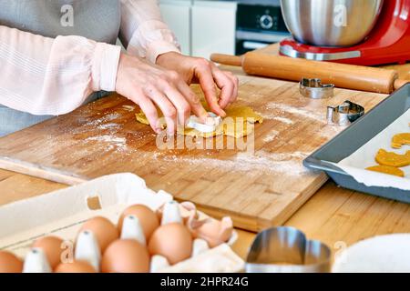 Die Hände der Frau schneiden Kekse in Form eines Herzens auf dem Tisch der Küche aus. Hausgemachtes Gebäck oder Kuchen. Kekse backen. Stockfoto