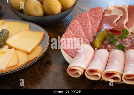 Platte aus Wurstwaren mit Raclettekäse und Kartoffeln auf einem Holztisch Stockfoto