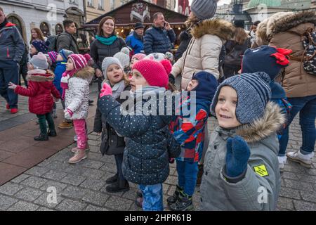 Junge Schüler, Lehrer, die sich die Krippen von Kraków Szopka angeschaut haben, die während des jährlichen Wettbewerbs im Dezember auf dem Adam Mickiewicz Denkmal, Hauptmarkt, Kraków, Polen, ausgestellt wurden Stockfoto