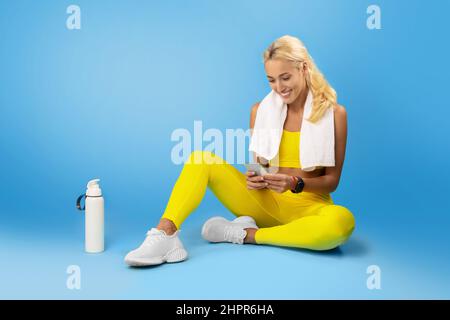 Sportlich lächelnde Frau, die im Studio ein Handy benutzt Stockfoto