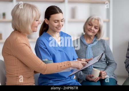 Hübsche junge Krankenschwester befragt ältere Damen im Pflegeheim Stockfoto