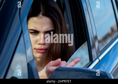 Aggressives Fahren. Weibliche verärgerte Fahrerin zeigt während der Fahrt eine Geste mit dem Mittelfinger. Stockfoto