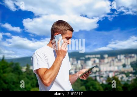 Hübscher junger Geschäftsmann, der vor dem Hintergrund der Panoramaaussicht auf die Stadt telefoniert. Stockfoto