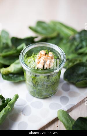 Grüner Nussbaum-Pesto in einem Glasgefäß, verziert mit einer Walnuss und verstreuten Blättern Stockfoto