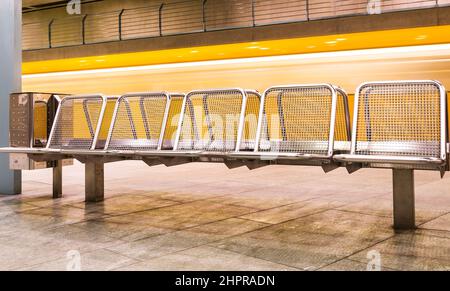 Yellow Train raste in der U-Bahn hinter metallenen Wartebänken Stockfoto