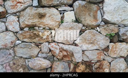 Eine alte Steinmauer im Dorf. Eine Steinwand aus Materialien verschiedener Größen. Vorderansicht und Nahaufnahme Stockfoto