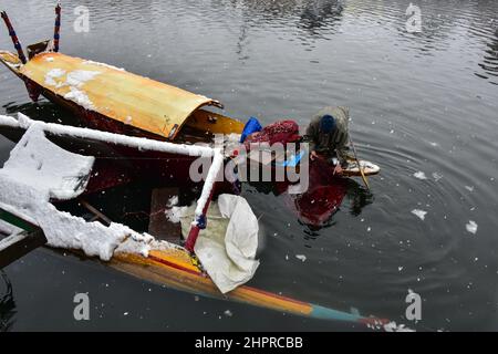 Kaschmir, Indien , 23/02/2022, Srinagar, Indien. 23rd. Februar 2022. Ein Mann inspiziert sein Boot, das durch starken Schneefall in Srinagar beschädigt wurde.die meisten Gebiete des Kaschmir-Tals erhielten am Mittwoch Schneefall - der erste schwere Sturz der Saison in den Ebenen - was den Flug- und Eisenbahnbetrieb störte und zur Schließung der lebenswichtigen Srinagar-Jammu-Nationalstraße führte, sagten Beamte hier. Kredit: SOPA Images Limited/Alamy Live Nachrichten Stockfoto