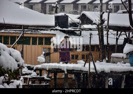 Kaschmir, Indien. 23rd. Februar 2022. Eine Frau räumt Schnee von einer hölzernen Fußbrücke während des starken Schneefalls in Srinagar. Die meisten Gebiete des Kaschmir-Tals erhielten am Mittwoch Schneefall - der erste schwere Sturz der Saison in den Ebenen - was den Flug- und Eisenbahnbetrieb störte und zur Schließung der lebenswichtigen Srinagar-Jammu-Nationalstraße führte, Beamte sagten es hier. Kredit: SOPA Images Limited/Alamy Live Nachrichten Stockfoto