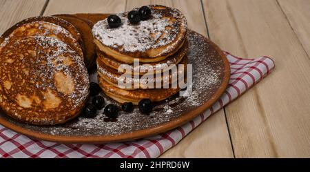 Pfannkuchen mit Beeren werden mit Zucker in einem Tonteller bestreut. Auf einem Tisch aus Holzbrettern. Stockfoto