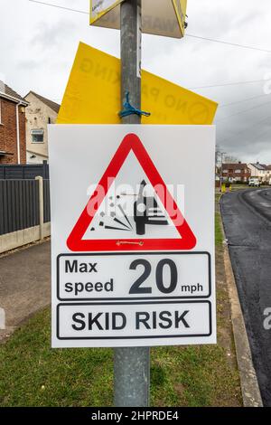Provisorisches Straßenschild an einem Laternenpfahl, das vor einem Schleuderrisiko warnt und ein Tempolimit festlegt. Stockfoto