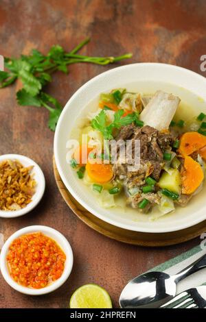 SOP Tulang Sapi oder indonesische klare Rindfleischsuppe, gemischt mit einigen Gemüsesorten wie Karotten, Kartoffeln, Kohl und grünen Bohnen. Serviert auf einer Keramikschale. Stockfoto