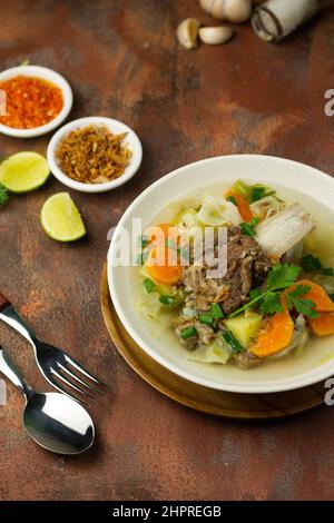 SOP Tulang Sapi oder indonesische klare Rindfleischsuppe, gemischt mit einigen Gemüsesorten wie Karotten, Kartoffeln, Kohl und grünen Bohnen. Serviert auf einer Keramikschale. Stockfoto