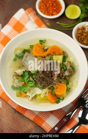 SOP Tulang Sapi oder indonesische klare Rindfleischsuppe, gemischt mit einigen Gemüsesorten wie Karotten, Kartoffeln, Kohl und grünen Bohnen. Serviert auf einer Keramikschale. Stockfoto