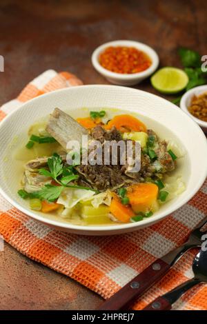 SOP Tulang Sapi oder indonesische klare Rindfleischsuppe, gemischt mit einigen Gemüsesorten wie Karotten, Kartoffeln, Kohl und grünen Bohnen. Serviert auf einer Keramikschale. Stockfoto