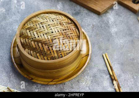 Bambus-Dampfgarer für Dim Sum oder chinesische Speisen mit Holzstäbchen. Grauer körniger Hintergrund. Selektiver Fokus. Platz für Text kopieren. Stockfoto