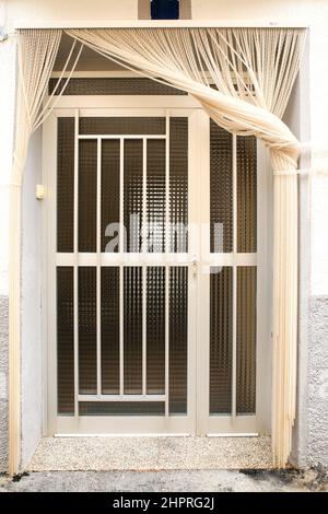 Weiße Aluminium-Tür mit geometrischen Details und weißem Vorhang Stockfoto