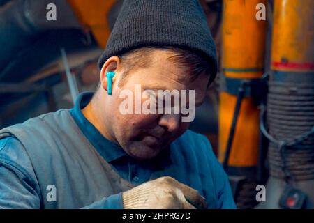 Porträt eines Schweißers in einem schwarzen Strickmütze auf dem Kopf am Arbeitsplatz mit einem Mikrofon im Ohr Stockfoto