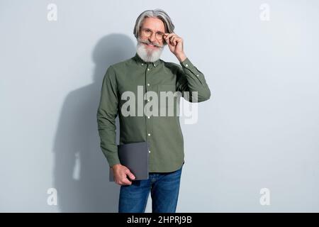 Porträt eines gutaussehenden trendigen, fröhlichen, erfahrenen intellektuellen grauhaarigen Mannes, der Laptop in der Hand hält, der isoliert auf einem Hintergrund in grauen Pastellfarben posiert Stockfoto