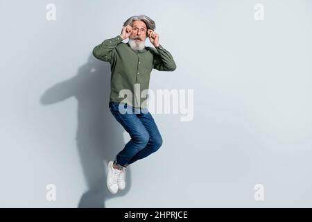 Foto von beeindruckt Mann Rentner verkleidet khaki Hemd Arme Hände Brille springen hoch isoliert grauen Hintergrund Stockfoto