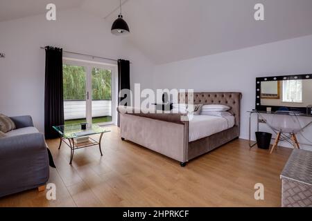 Swavesey, Cambridgeshire - August 22 2018: Schönes, modernes Luxus-Schlafzimmer mit schräg gewölbter Decke, eingerichtet mit begehrtem Sofa, Schlittenbett und Stockfoto