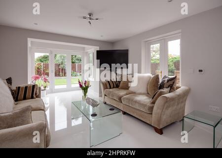 Swavesey, Cambridgeshire - August 22 2018: Atemberaubendes Wohnzimmer mit gläsernen Couchtischen, glänzendem weißem Porzellan-Fliesenboden, weißen Wänden, Sofas mit d Stockfoto