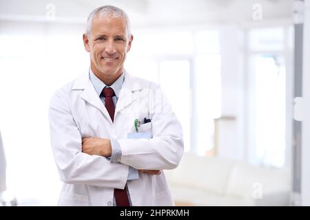 Ihre Gesundheit ist meine oberste Priorität. Porträt eines reifen Arztes, der mit gekreuzten Armen steht. Stockfoto