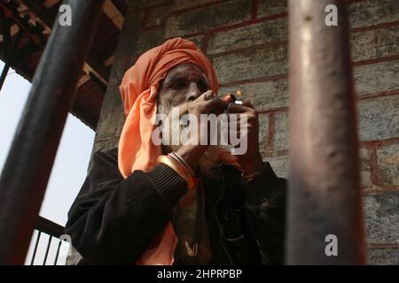 Kathmandu, Nepal. 23rd. Februar 2022. Ein Sadhu, ein Anhänger von Lord Shiva, raucht Marihuana aus einer Pfeife aus Lehm im Pashupatinath-Tempel, dem UNESCO-Weltkulturerbe, vor dem bevorstehenden Maha Shivaratri-Festival in Kathmandu, Nepal, am 23. Februar 2022. Maha shivaratri, ein Festival, das Lord Shiva gewidmet ist. Sadhus aus Nachbarländern sind vor dem bevorstehenden Maha Shivaratri Festival angekommen. (Foto: Abhishek Maharjan/Sipa USA) Quelle: SIPA USA/Alamy Live News Stockfoto