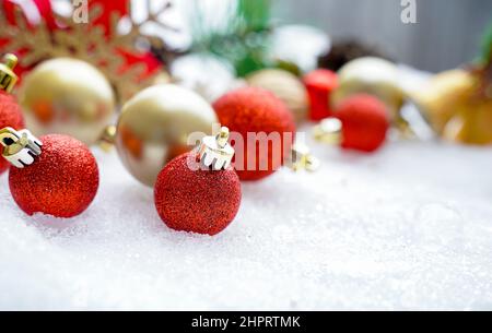 Weihnachten des Winters - Weihnachtskugeln mit Band auf Schnee, Winterurlaub Konzept. Weihnachtliche rote Kugeln, goldene Kugeln, Kiefer und Schneeflocken Dekoration Stockfoto