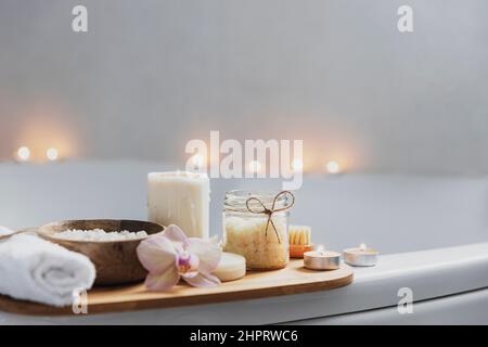 Vorbereitung für Hotel-Spa-Behandlung, Home-Bad Verfahren. Weißes Waschbecken im Badezimmer, Accessoires auf Tablett. Brennende Kerzen, Seife, Fußbürste, Handtuch, Glasflasche mit Meersalz, Orchideenblume Stockfoto