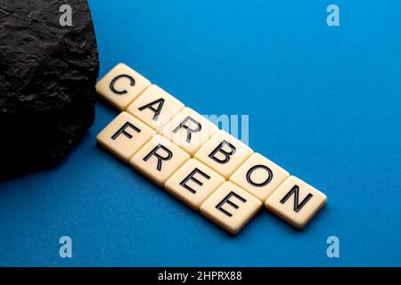 Ein Kohleklumpen auf blauem Hintergrund mit dem Satz „kohlenstofffrei“, der aus Buchstaben besteht. Foto aufgenommen unter künstlichem, weichem Licht Stockfoto