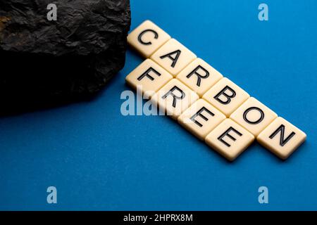 Ein Kohleklumpen auf blauem Hintergrund mit dem Satz „kohlenstofffrei“, der aus Buchstaben besteht. Foto aufgenommen unter künstlichem, weichem Licht Stockfoto