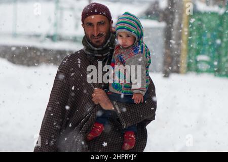 Srinagar, Indien. 23rd Januar 2022. Ein Mann, der am 22. Februar 2022 in Srinagar, Kaschmir, Indien, einen Sohn bei einem starken Schneefall hält. (Fotos von Faisal Bashir/INA Photo Agency/Sipa USA) Quelle: SIPA USA/Alamy Live News Stockfoto