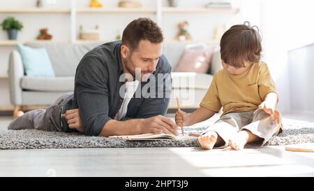 Frühzeitige Bildung. Netter kleiner Junge, der zu Hause mit Papa zeichnet, liebevoller Vater, der seinem Kind beibringt, Briefe zu schreiben, Panorama Stockfoto