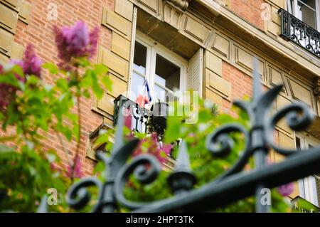 Frühling in Paris. Blühende Fliederblumen und ein typisches Pariser Gebäude mit französischer Flagge, die aus dem Fenster hängt. Selektiver Fokus auf das Gebäude. Stockfoto