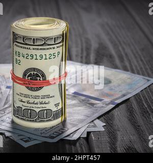 Eine Rolle von Dollarscheinen und Münzen über andere Scheine auf einem Schreibtisch. Highlight für die 100-Dollar-Rechnung. Stockfoto