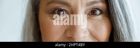 Fröhliche silberhaarige Dame mit Make-up schaut in die Kamera auf hellgrauem Hintergrund Stockfoto