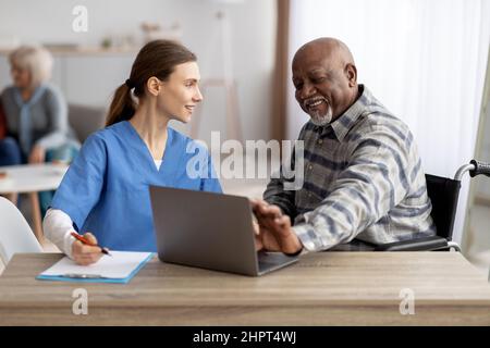 Freundliche Krankenschwester, die älteren schwarzen Patienten mit einem Laptop hilft Stockfoto