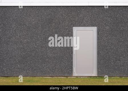 Eine graue Sicherheitstür auf einem dunkelgrauen Betongebäude mit Rasen im Vordergrund, Frederikssund, Dänemark, 22. Februar 2022 Stockfoto