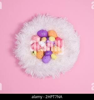 Bunte Ostereier in kreativem flauschigen, umweltfreundlichen Fell nisten auf pastellrosa Hintergrund. Grußkarte mit flachem Lay-Papier und minimalem Kopierplatz Stockfoto