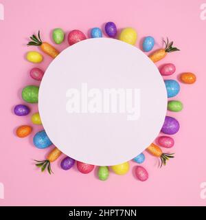Bunte Osterschmuck unter runden Papierkarten-Kopierfläche auf pastellrosa Hintergrund. Kreative Grußkarte flach legen Stockfoto