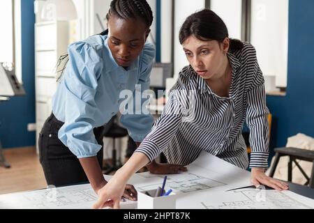 Engagiertes Team von Ingenieuren Kollegen diskutieren Baupläne stehen am Schreibtisch in modernen Architekturbüro. Team von zwei Architektinnen diskutiert Baupläne für Stadtentwicklungsprojekt. Stockfoto