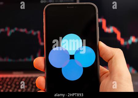 OKB-Kryptowährung-Logo auf dem Bildschirm des Smartphones in mans-Hand mit Abwärtstrend auf dem Chart auf rotem Hintergrund, Februar 2022, San Francisco, USA. Stockfoto