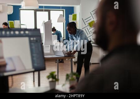 Architekt mit Blick auf Entwürfe auf Laptop am Schreibtisch mit Architekturmodell von Bürogebäuden. Ingenieur, der mit Computer arbeitet, um ein modernes Designkonzept für ein städtisches Wohnprojekt zu schaffen. Stockfoto