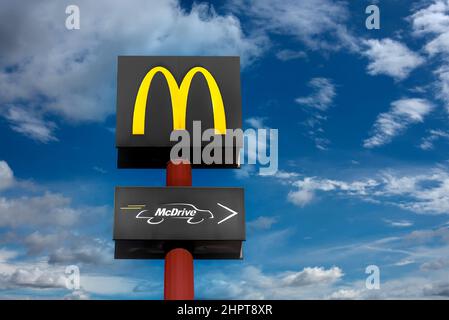 Fossano, Italien - 22. Februar 2022: McDonald's Restaurant-Logo und McDrive-Logo auf rotem Pol über blauem Himmel mit Wolken. Es ist das LAR der Welt Stockfoto