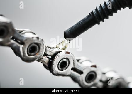 Schmieren einer Fahrradkette mit einem Tropfen goldenem Öl aus nächster Nähe auf grauem Hintergrund. Pflege des Fahrradantriebs. Stockfoto