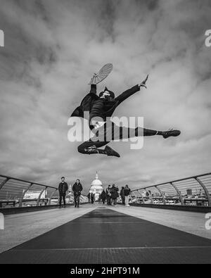 Ein schwarz-weißes Bild eines Kampfkünstlers und eine Tänzerin spielt auf der Millennium Bridge in London hohe Tritte. Stockfoto