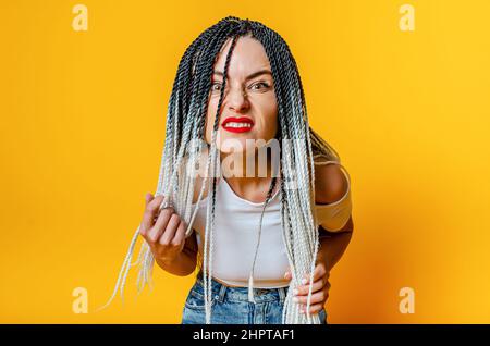 Porträt einer wütenden Frau mit Dreadlocks. Hände halten Dreadlocks. Sich nach unten lehnen, um die Kamera zu betrachten. Stockfoto
