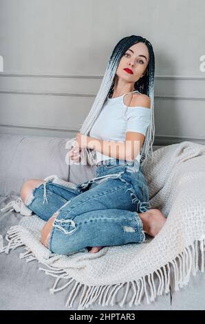 Gemütliche Erholung. Junge Frau, die sich auf der Couch ausruhte. Stylischer Look. Lange Afrogeflechte Stockfoto