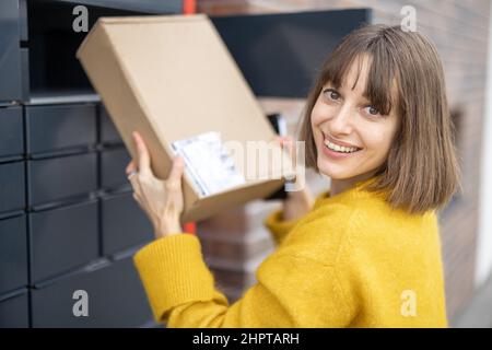 Frau bekommt Paket aus der Zelle des automatischen Postterminals im Freien Stockfoto