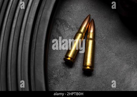 Zwei Kugeln und Kalaschnikow-Sturmgewehr auf grauem Betongrund, Draufsicht. Cartridge 7,62 Kaliber für ak 47 Closeup Stockfoto